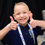 A child gives a smiling thumbs up to the camera. 