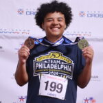 A teenager smiles while holding his medals. 