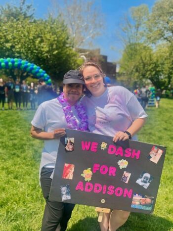 Two women hold a sign and pose for a picture.